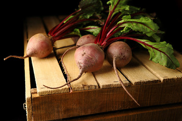 A bunch of fresh beets with tops on an old, wooden drawer. illuminated by light. New harvest.