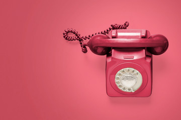 Red vintage antique rotary phone on a pink background shot from above with copy space and room for...