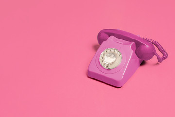 Pink vintage antique rotary phone on a pink background with copy space and room for text with a...
