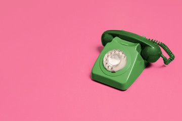 Green vintage antique rotary phone on a pink background with copy space and room for text with a...