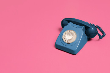 blue vintage antique rotary phone on a pink background with copy space and room for text with a...