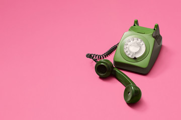Green vintage antique rotary phone with lifted handset receiver on a pink background with copy...