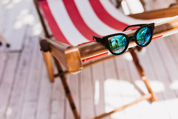 Sparkle female sunglasses lying on striped recliner. Photo of elegant summer glasses on...
