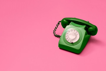 Green vintage antique rotary phone on a pink background with copy space and room for text with a right side composition.