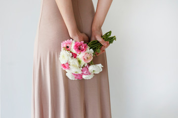 Conceptual image of a woman wearing fashionable beige dress holding spring flowers. Female with colorful white and pink ranunculus bouquet over white background. Close up, copy space, cropped shot.