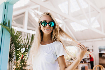 Wonderful laughing girl touching her long blonde hair during photoshoot in cafeteria. Cheerful...