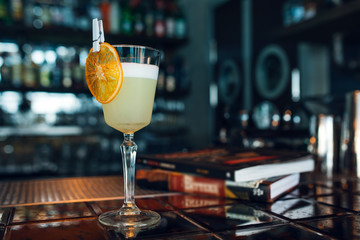 Pisco Sour cocktail with dried orange slice at bar or restaurant background. Closeup.
