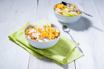 Granola and vegetarian yogurt with slices of apple, apricot, banana on a white wooden background. Two plates of oatmeal