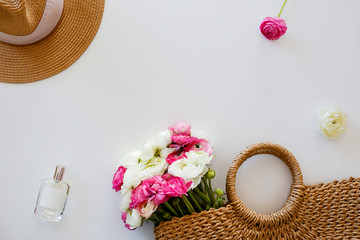 Conceptual image of woman's fashionable wicker bag with spring flowers. Colorful white and pink ranunculus bouquet over white background. Close up, copy space, cropped shot.