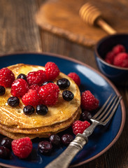 Sweet homemade pancakes with raspberries and blueberries on blue plate.