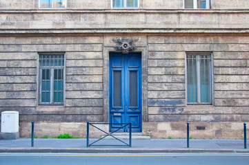 Fototapeta na wymiar High blue wooden door with two narrow windows on the grey building facade