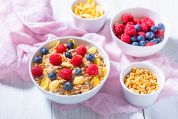 Bowls with granola, blueberries and raspberries, cornflakes and puffed rice on a wooden background. Healthy breakfast