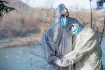 man and woman in protective cloths hugging. man look into a camera.