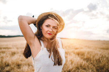 beautiful girl in a hat with brunette hair on a wheat field background. warm summer time. 