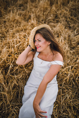 beautiful girl in a hat with brunette hair on a wheat field background. warm summer time. 