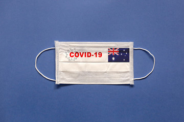 Flag of Australia and inscription COVID-19 on a medical mask on a blue background. Healthcare and medical concept. Pandemic virus COVID-19