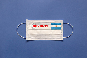Flag of Argentina and inscription COVID-19 on a medical mask on a blue background. Healthcare and medical concept. Pandemic virus COVID-19