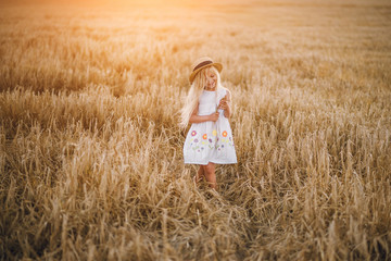 Fototapeta na wymiar beautiful little girl in a hat with blond hair on a wheat field background
