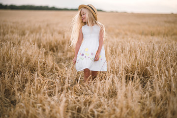 beautiful little girl in a hat with blond hair on a wheat field background