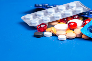 Disposable medical mask and blister with white pills lie on a blue background