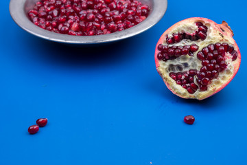 Pomegranate grains in a metal plate and half ripe pomegranate on a blue background