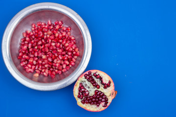 Pomegranate grains in a metal plate and half ripe pomegranate on a blue background
