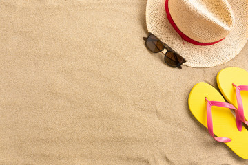 Fototapeta na wymiar Straw hat and flip flops, on sand background. Beach vacation concept .Top view with copy space.