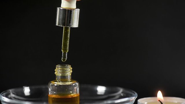 Aromatherapy, the creation of spirits. Butter with a pipette, drop drops. Spa, burning candle, dark background.
