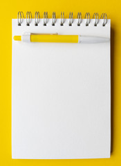 Blank sheet of notebook with pen on it. Educational concept in yellow and white colors. Stock photography.
