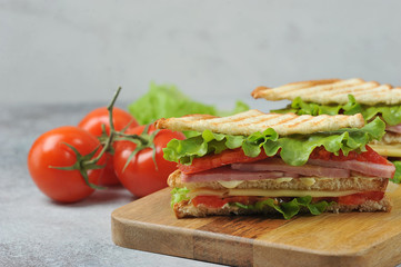 Classic club sandwich on a wooden tray.  The delicious sandwich filling consists of ham, cheese, sliced ​​tomato, lettuce and sauce.  In the background are tomatoes and lettuce.  Close-up.