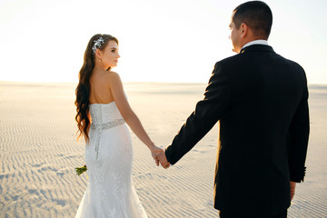 The bride and groom walk in the desert, the guy leads the girl along the dunes of the desert