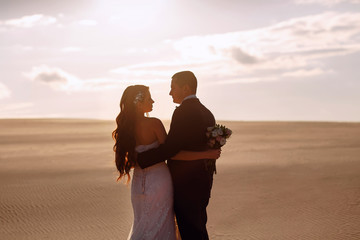 Bride and groom cuddle in the desert against sunset