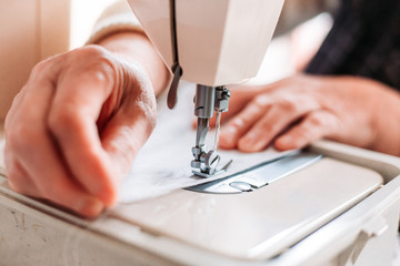 Womans hand sewing on the sewing mashine homemade medical mask.