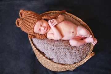 A newborn boy in a knitted hat, sleeping on a blanket lies in a basket.