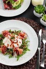 burrata cheese with Italian delicatessen salad with parma ham slices on white plate on rustic...