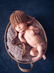 A newborn boy in a knitted hat, sleeping on a blanket lies in a basket.