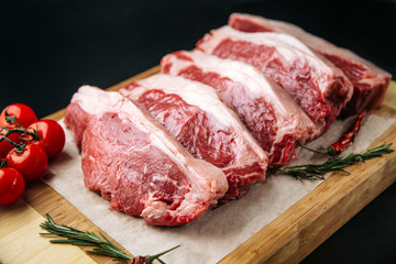 Raw uncooked meat steak striploin new york on a wooden board with tomatoes and rosemary, side view, horizontal