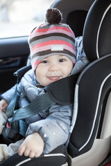 Happy and smiling toddler sitting in baby car seat on back of the car