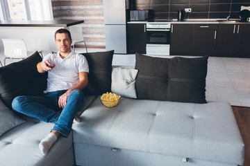 Young man watch tv in his own apartment. Joyful happy attractive ordinary guy hold remote control with straightened hand. Switching tv channels. Entertain himself at home.