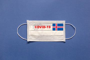 Flag of Iceland and inscription COVID-19 on a medical mask on a blue background. Healthcare and medical concept. Pandemic virus COVID-19