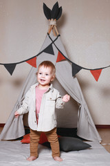 A child, a boy, is sitting and playing in a tent inside the house on a wooden background. © Aleksei Zakharov