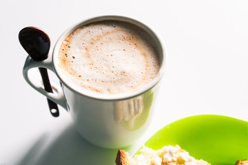 Cup of white coffee with a spoon and a plate with the lunch