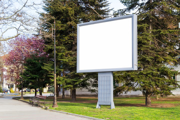 Blank billboard mockup with copy space in a pablic park on a spring day. Empty banner for advertisement. Large white screen for your text.