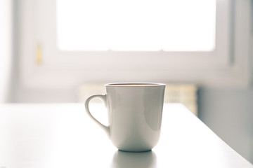 White coffee mug on a white desk with the light from a window