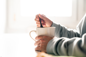 Person stirring a coffee cup with a ceramic spoon. One person's hands.