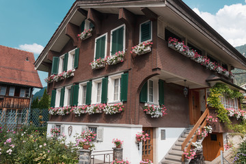 Beautiful traditional wooden house in the alpine village, Switzerland. House decorated with flowers, near flowerbed.