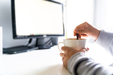 Person stirring a coffee in front of the computer on a desk.