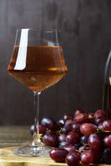 A glass filled with rose wine and a bunch of red grapes are nearby. Close-up. Vertical orientation