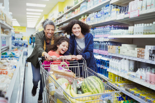 Playful multi-generation women pushing shopping cart in supermarket