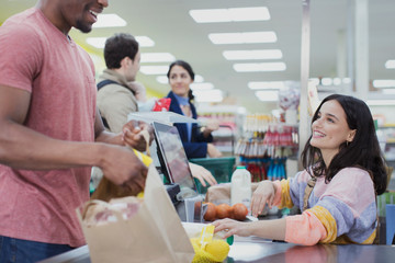 Friendly cashier helping customers at supermarket checkout